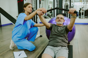 Paciente mayor realizando ejercicios de rehabilitaci&oacute;n con ayuda de una profesional de la salud