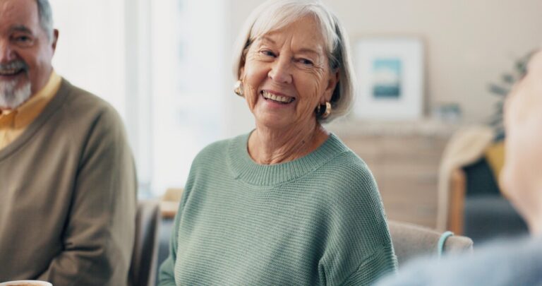 Mujer mayor sonriendo en un entorno acogedor con otros mayores