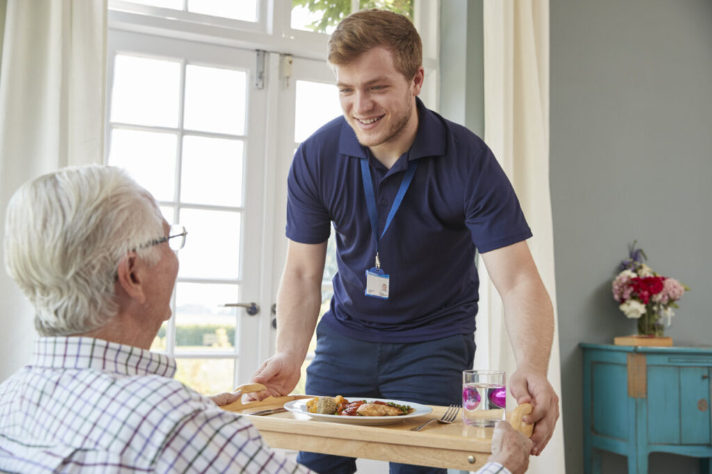 Un cuidador sonriente sirviendo comida a un anciano en casa