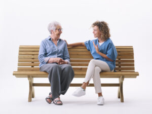 Una mujer mayor y una cuidadora conversando en un banco de madera.