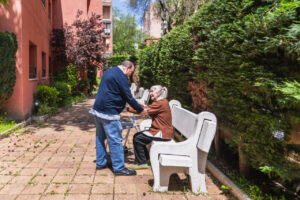 Persona mayor interactuando con un cuidador en un jard&iacute;n de residencia