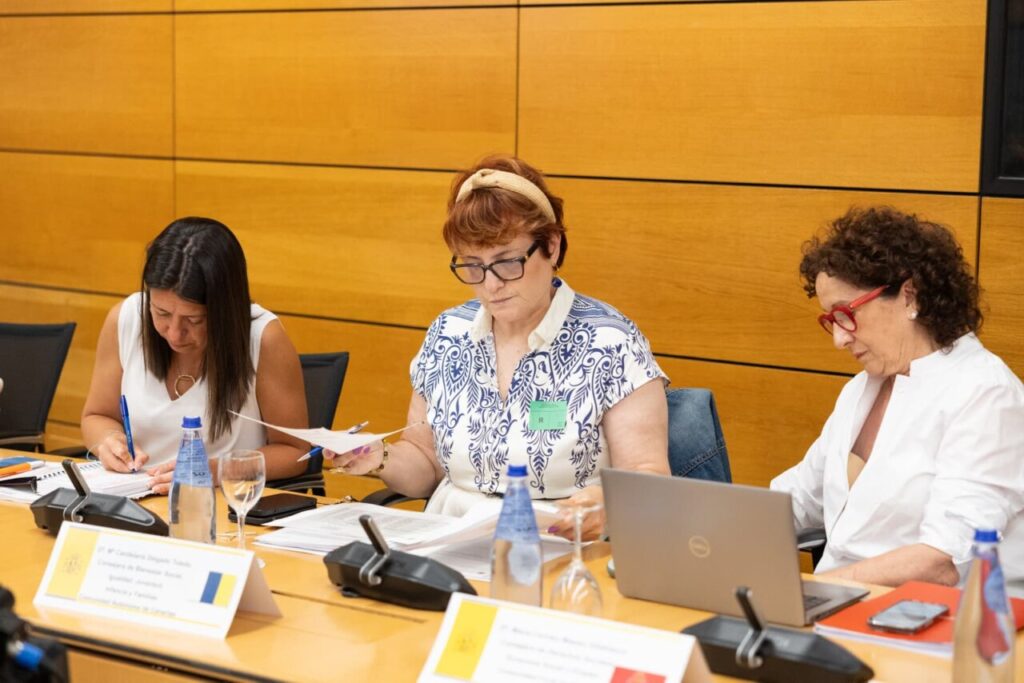 Tres mujeres en una reunión sobre dependencia, tomando notas y revisando documentos.