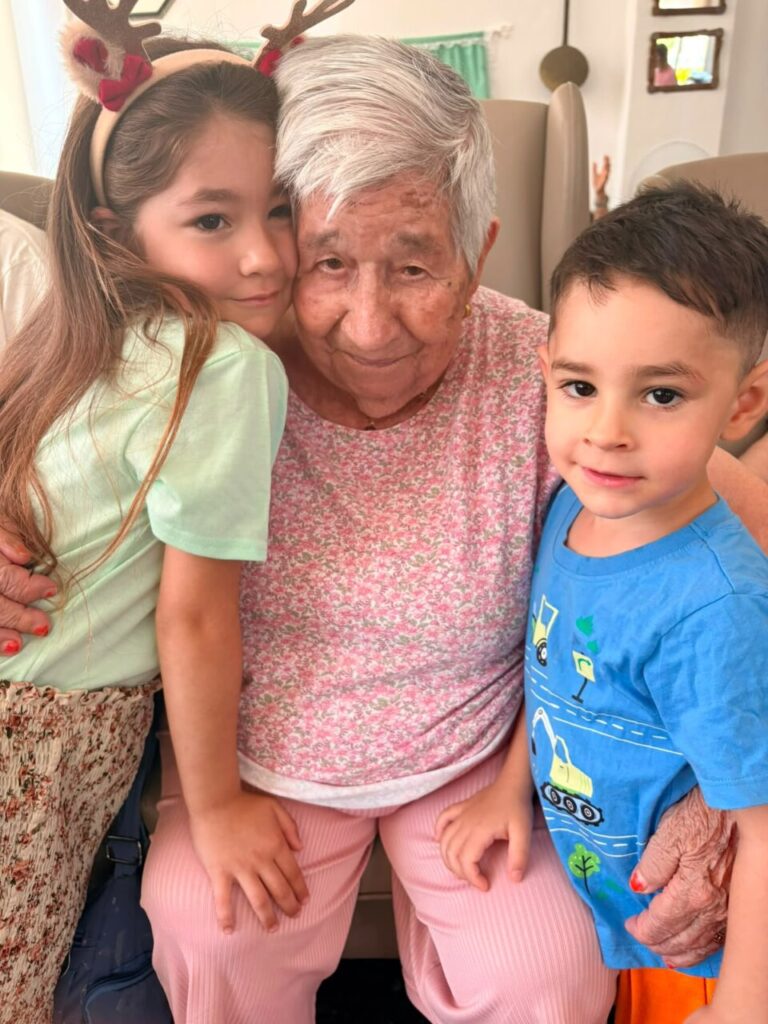 Abuela abrazada por dos niños en celebración del Día de los Abuelos