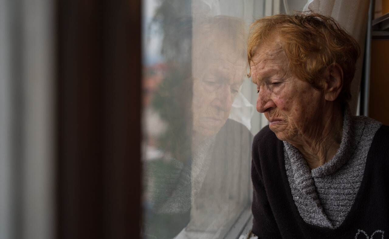 Mujer mayor mirando por la ventana con expresión reflexiva
