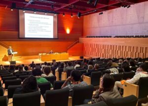 Público escucha una ponencia en un auditorio con una diapositiva sobre el delirium