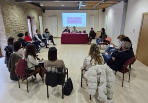 Varias personas sentadas en círculo participan en una reunión con una presentación proyectada.