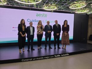 Seis personas posan en un escenario ante una pantalla de AESTE y Cuidar es futuro.